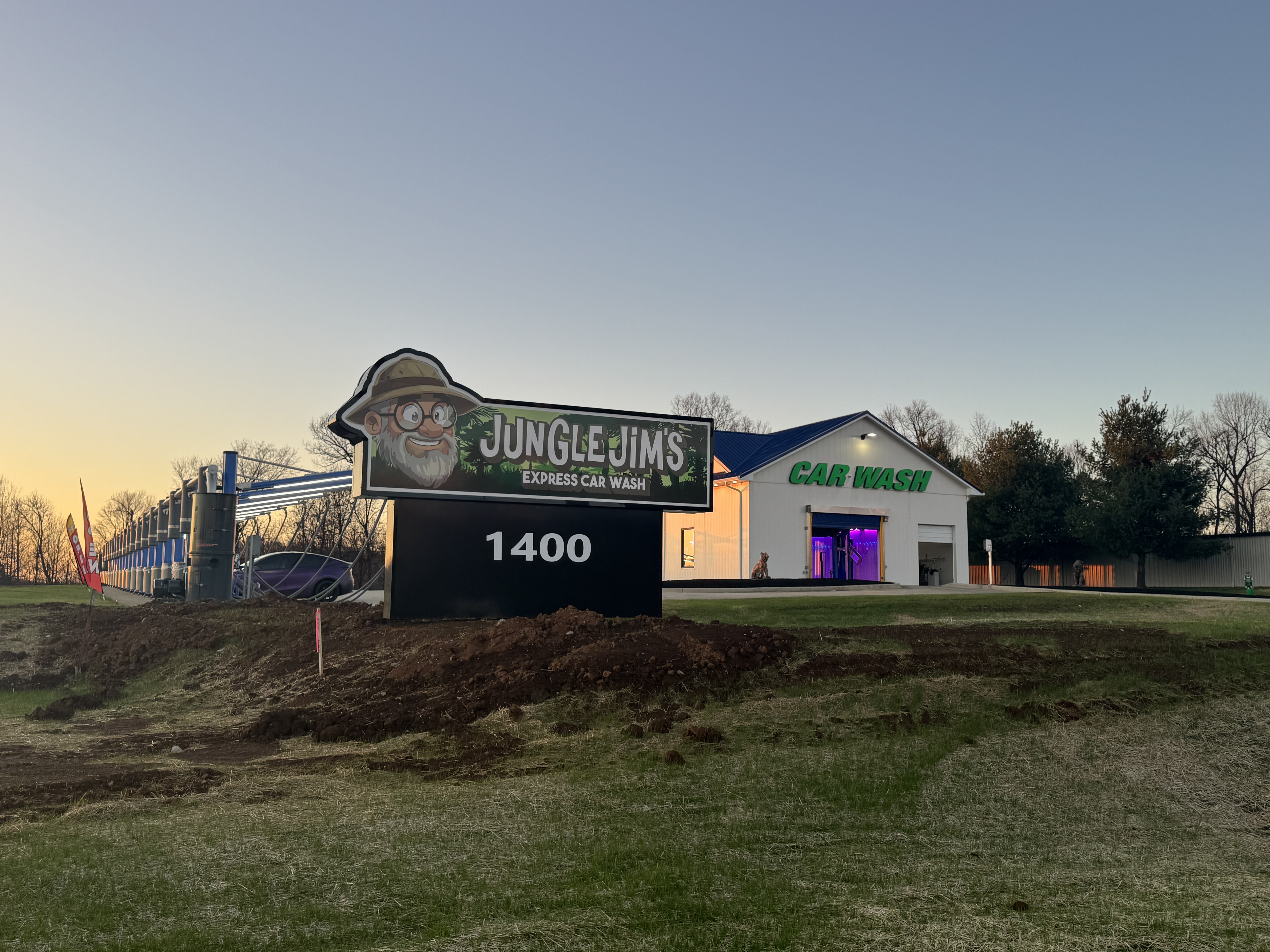 Jungle Jim's Express Car Wash exterior viewed from the road with purple tunnel lighting at dusk